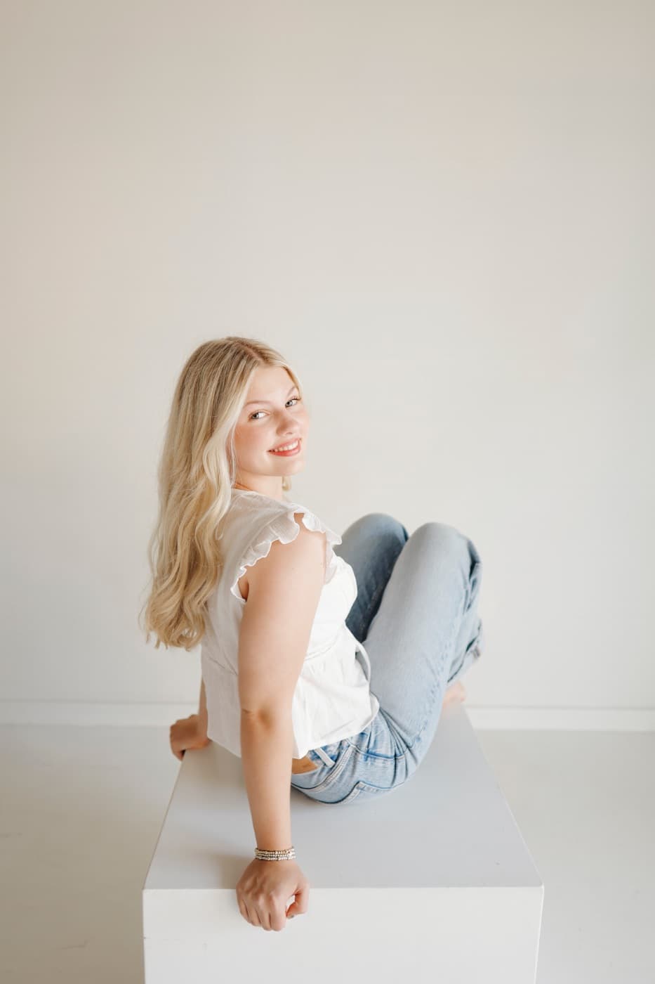 A woman sitting on a white posing block against a white wall