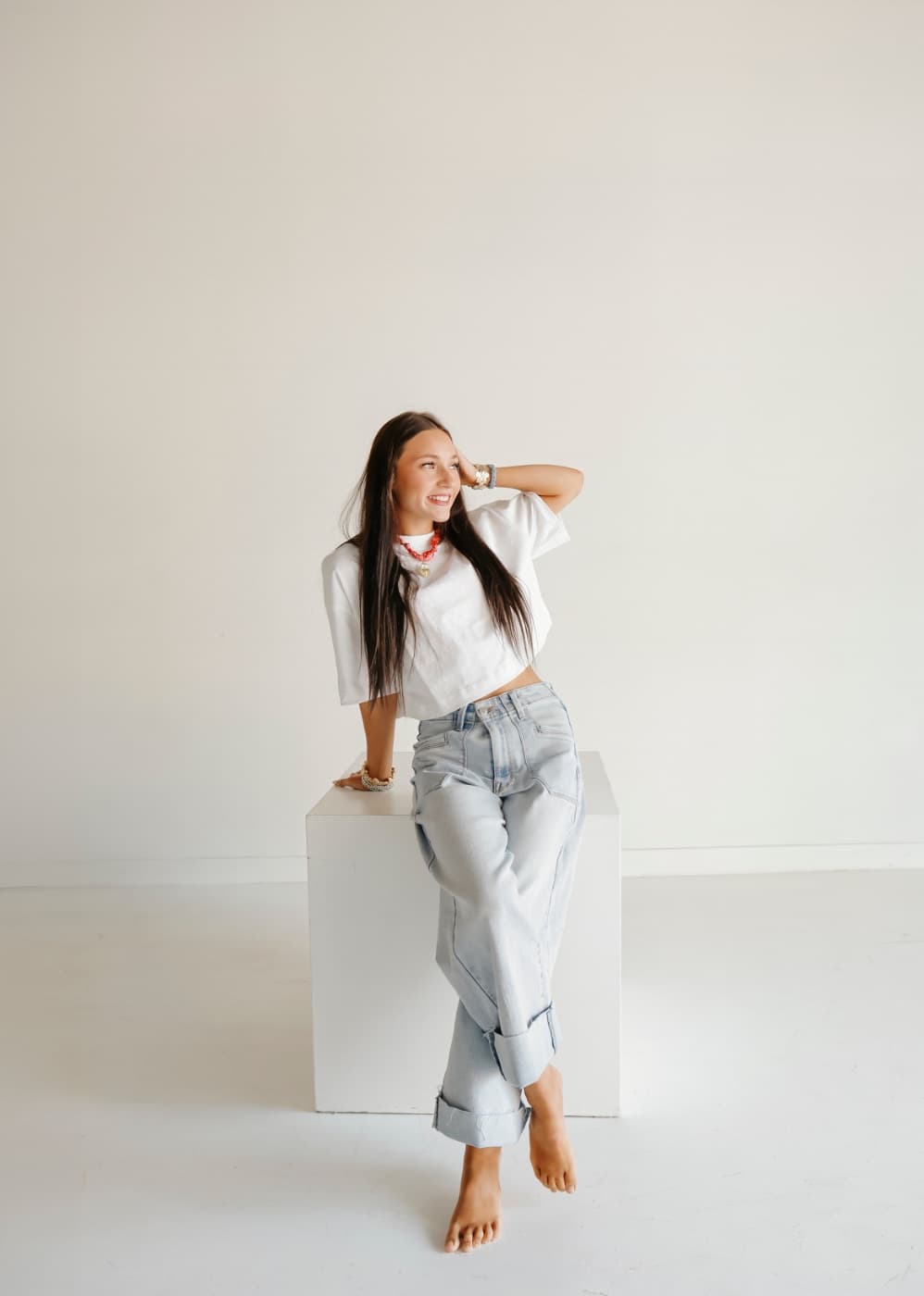A woman in a white tee and jeans sitting on a white posing block